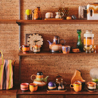 shelves of brightly coloured 70s ceramics from hkliving with jugs and kettles among the cups and mugs