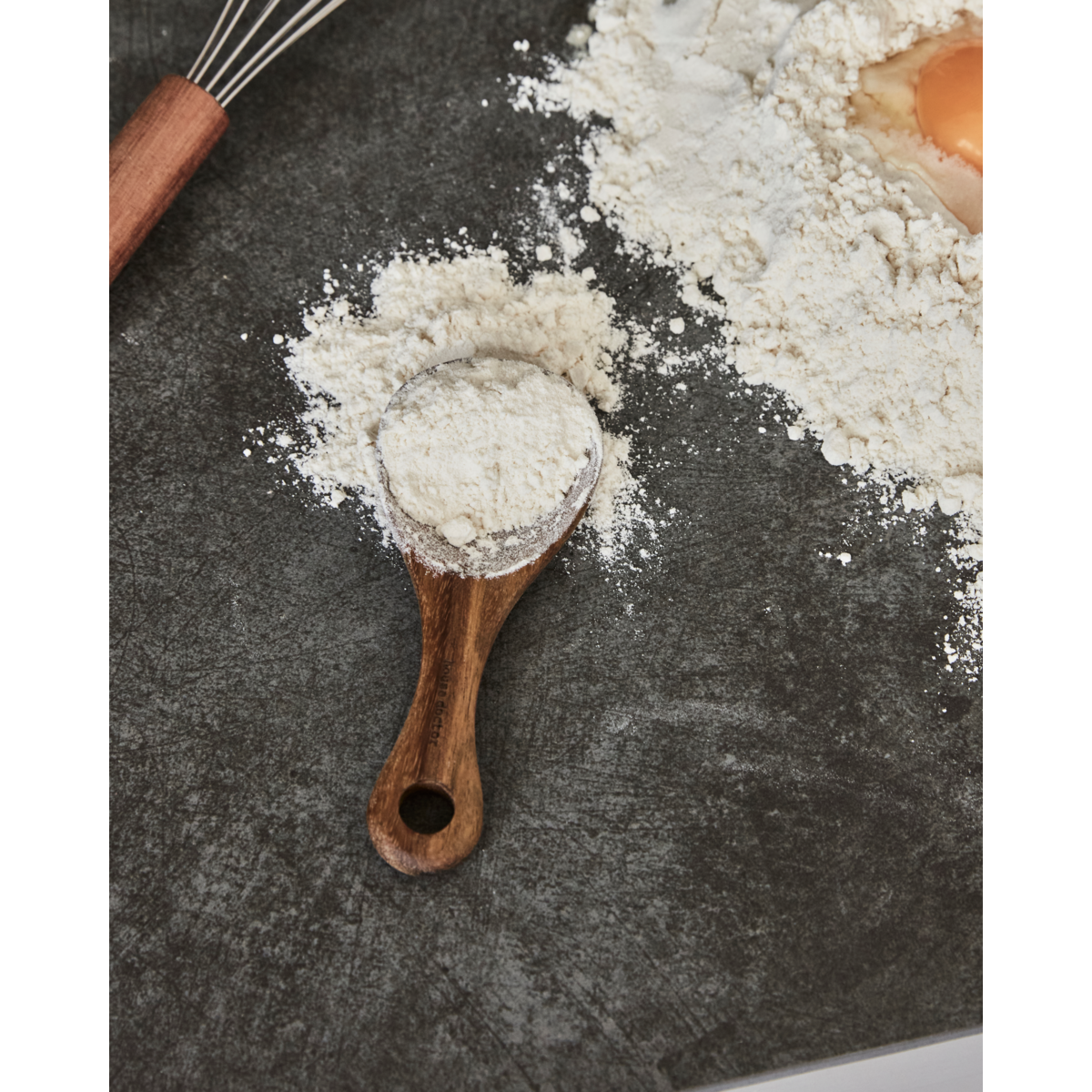 Acacia wood scoop spoon resting on dark countertop with flour – rustic kitchen tool