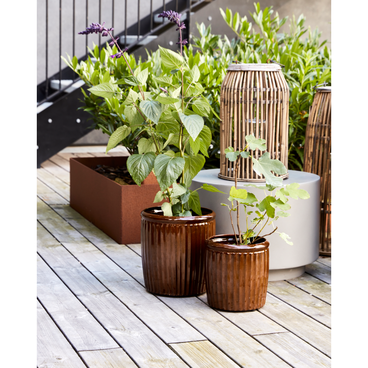 Large and small ribbed outdoor planters on wooden deck with greenery