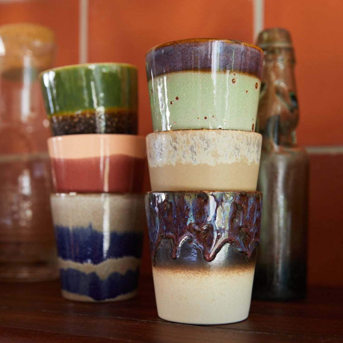 a selection of mugs from the hkliving colourful 70s collection sat on a kitchen worktop with terracotta tiles int he background