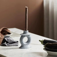 stone candle holder with coffee coloured taper candle that has burnt a quarter way down on a table in a kitchen