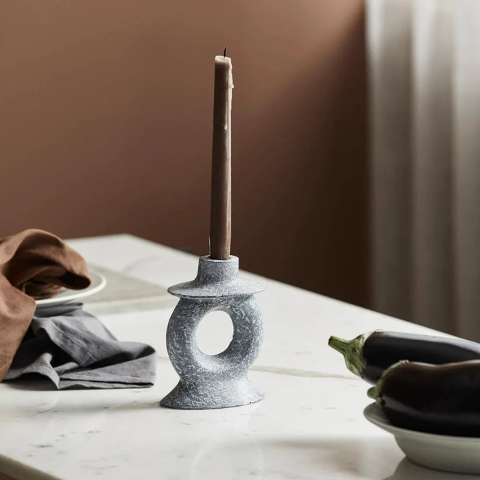 stone candle holder with coffee coloured taper candle that has burnt a quarter way down on a table in a kitchen