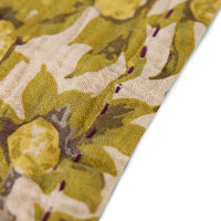 close up of the corner of a cloth napkin from hkliving with a fruiting branch style in yellow, green, and beige, with a purple stitching around the outeredge
