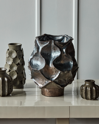 Large House Doctor HDWaves vase in antique metallic glaze styled on a console with other ceramics.