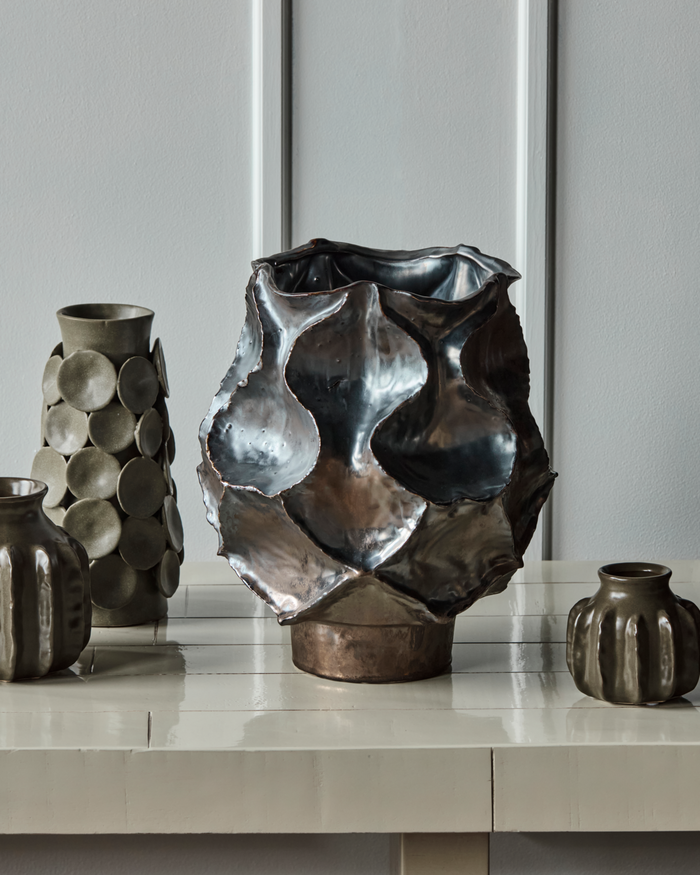 Large House Doctor HDWaves vase in antique metallic glaze styled on a console with other ceramics.