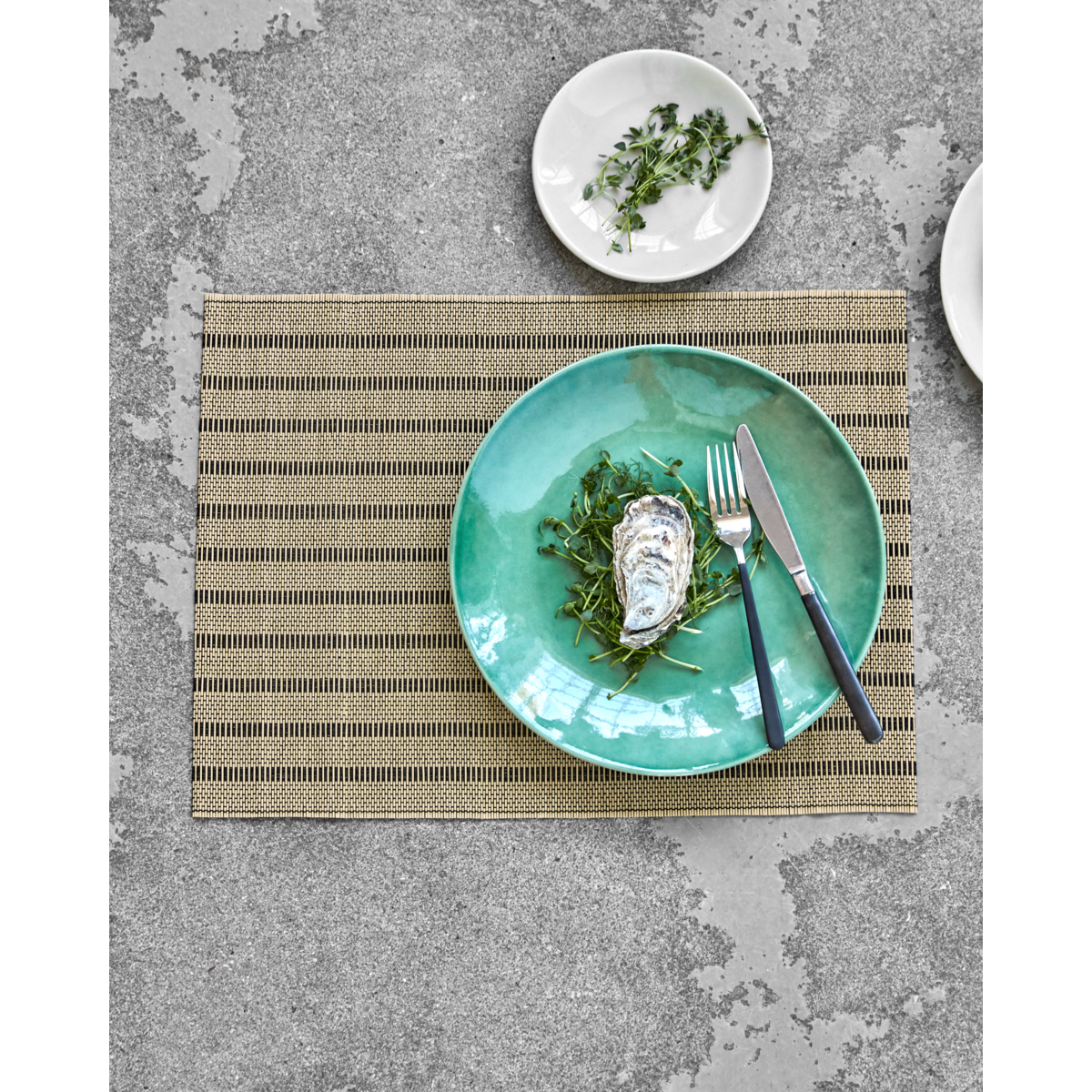 Placemat styled with green plate and cutlery on concrete surface