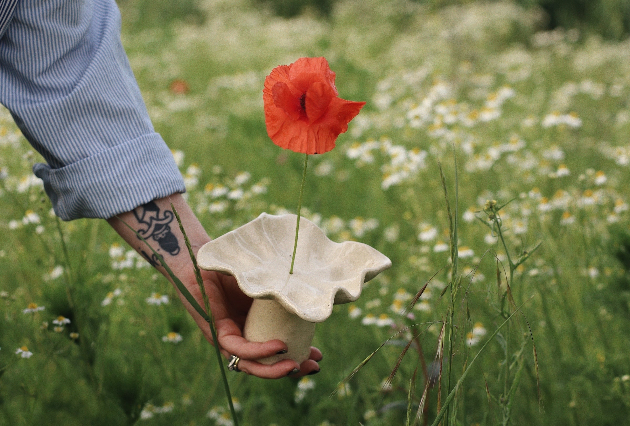 Hand holding a handmade ceramic incense holder by Leeds-based ceramicist Lee Simmonds, with a single red poppy, in a wildflower field