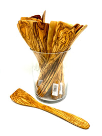 Glass jar filled with olive wood spatulas with one spatula in the foreground