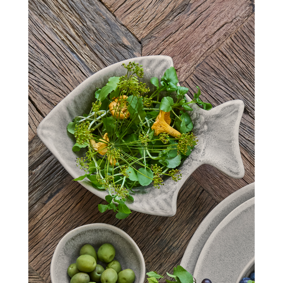 Fish-shaped bowl filled with greens and chanterelles on wooden table