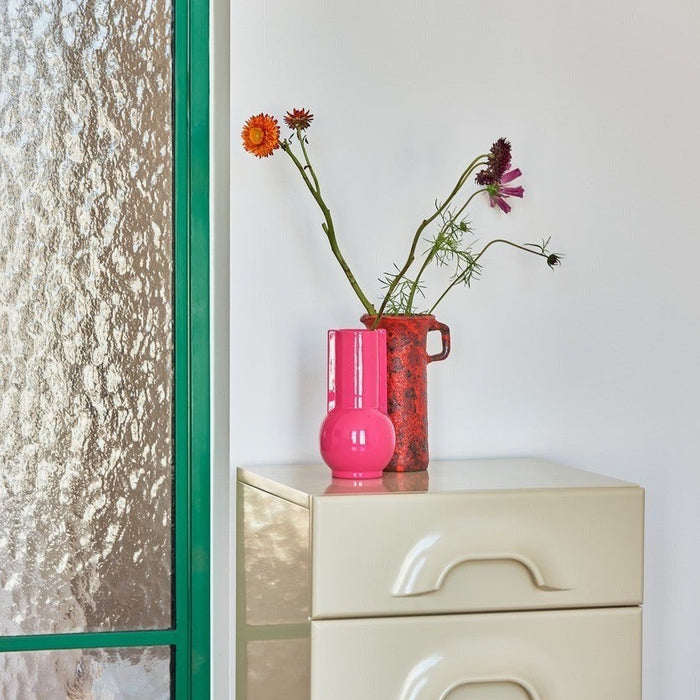 tall hot pink vase on a beige chest of drawers with a red jug all from hkliving