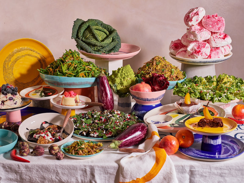 a table bowing under the weight of a feast for both the eyes and the stomach with bright and cheerful colours coming from both the food and the plates of the ottolenghi feast collection by serax