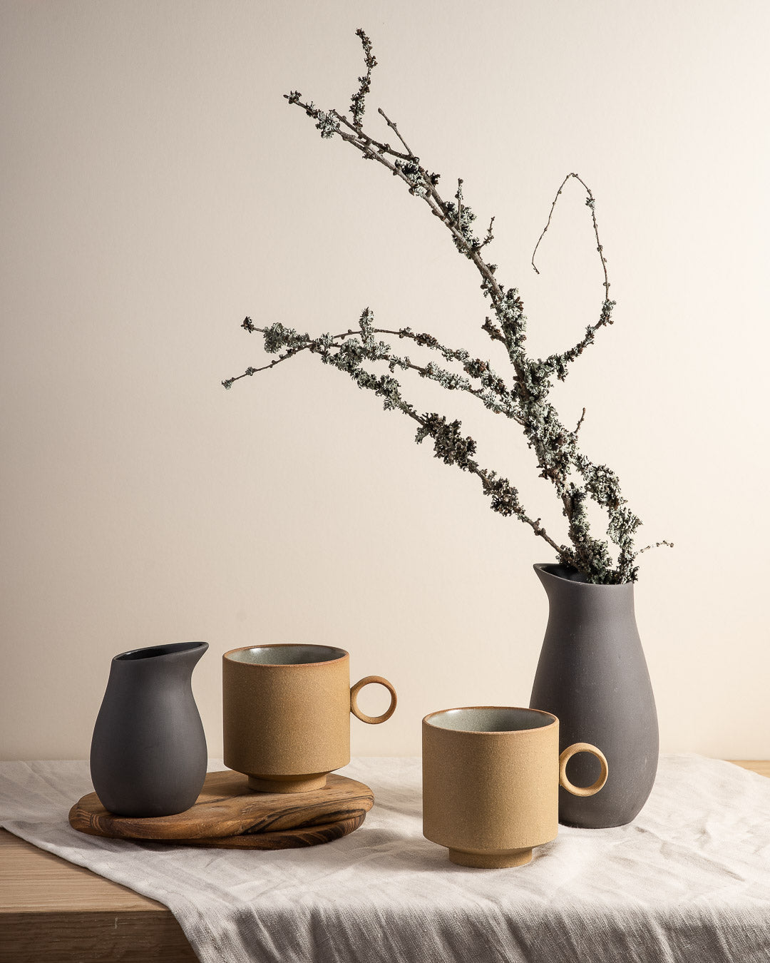 and table with a small runner across it, with a couple of born mugs with unusually round handles and 2 grey vases that look almost like birds stood with their beaks pointing skywards