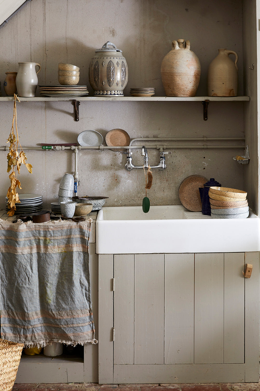 a kitchen sink area with shelves above it holding jars and plates with a kitchen towel hanging over the side