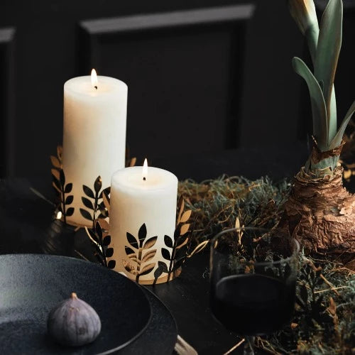 cream pillar candles in a display on a table with woodland foliage, a sprouting amarylis, and an almost finished glass of red wine