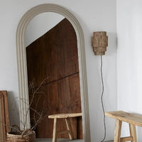 the wall sconce attached to a plain wall with a large round topped mirror resting next to it