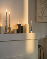 two cream ceramic candlesticks shaped like fish, each holding a lit cream taper candle, on a small round table with papers and matches