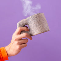 Seletti Newlithic mug in speckled stone-look porcelain, held in hand, steaming hot drink
