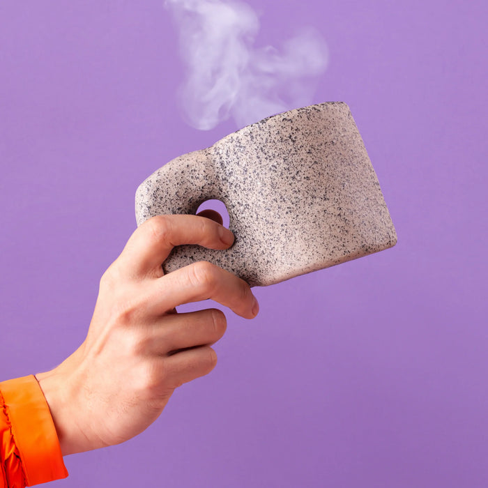 Seletti Newlithic mug in speckled stone-look porcelain, held in hand, steaming hot drink
