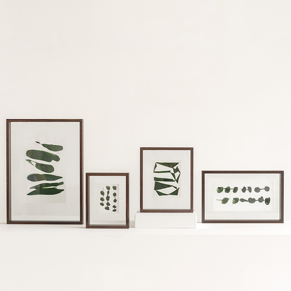 collection of walnut floating frames with green abstract prints styled on a shelf
