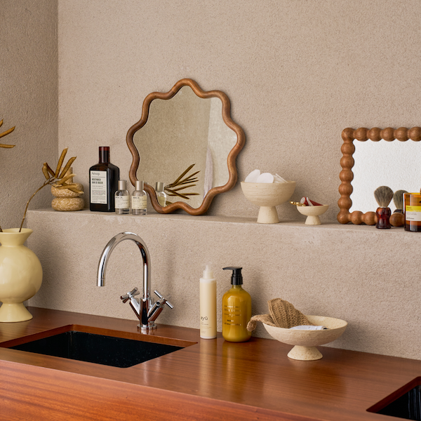 Bathroom counter with sink, mirror, and various items on a neutral wall.
