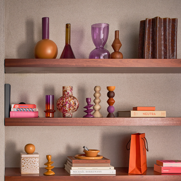 Decorative shelves with various colorful vases and objects from Urban Culture Nature Amsterdam, books, and a bag against a neutral wall.
