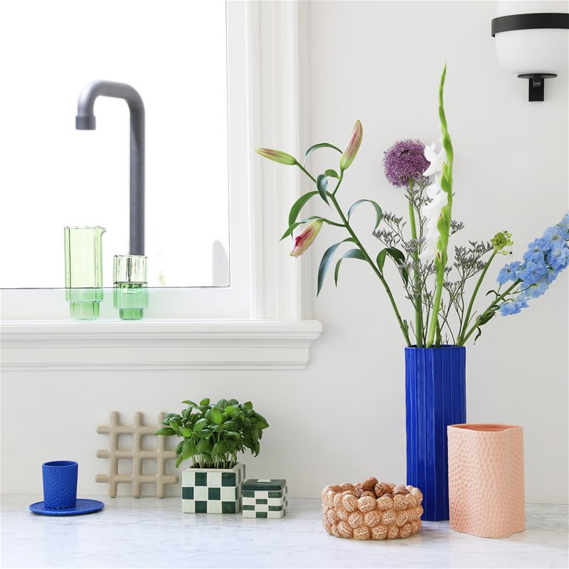 beige speckled grid trivet styled in a bright modern kitchen with plants and colourful ceramics
