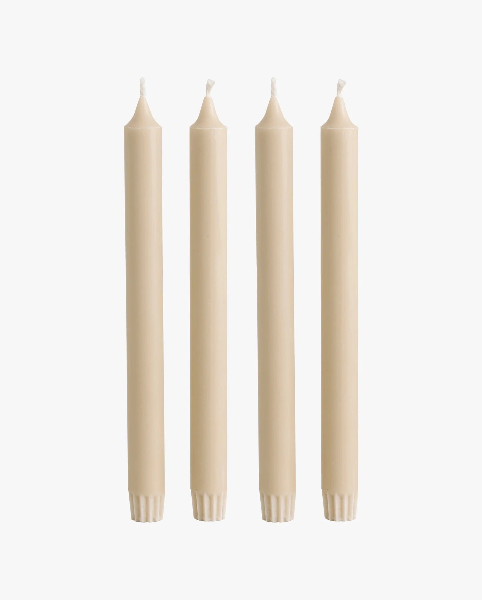 row of lit candles on a white mantelpiece shelf: two ceramic fish-shaped candlesticks holding cream taper candles, a cluster of cream and dark olive green pillar candles of varying heights, and a brass candlestick holding another taper candle, with framed artwork on the wall behind