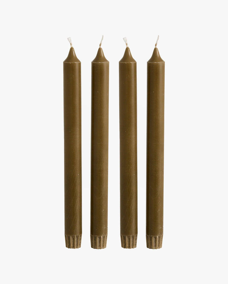 row of lit candles on a white mantelpiece shelf: two ceramic fish-shaped candlesticks holding olive green taper candles, a cluster of cream and dark olive green pillar candles of varying heights, and a brass candlestick holding an olive green taper candle, with framed artwork on the wall behind