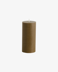 lit dark olive green and cream Nordal pillar candles on a white radiator cover, with a spiky cream ceramic dish, a dark textured rock ornament and a matchbox alongside