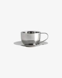 Close-up of the VIREA chrome cup and saucer by Nordal with coffee, on a dark wood table