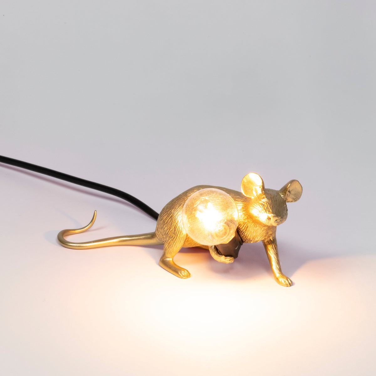 Seletti Gold lying down Mouse Lamp switched on, with a warm glowing bulb