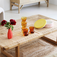 pastel pink ceramic jar with yellow lid styled on a woven coffee table with amber glasses by &klavering amsterdam
