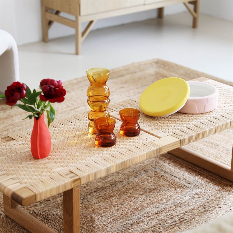 pastel pink ceramic jar with yellow lid styled on a woven coffee table with amber glasses by &klavering amsterdam
