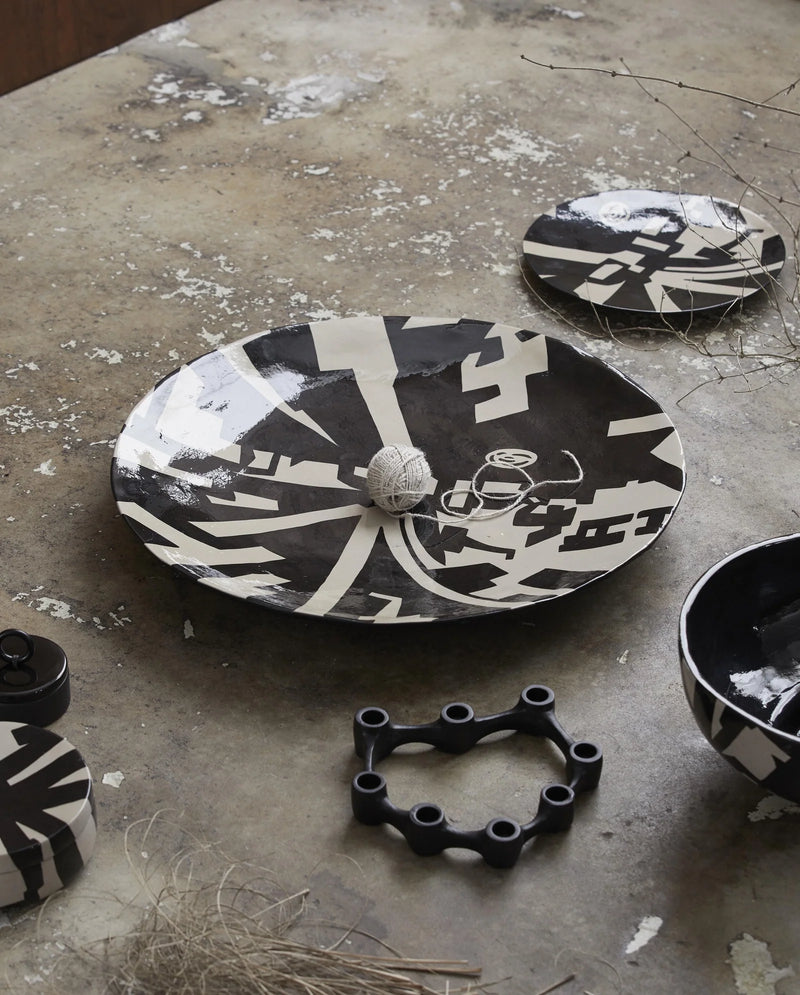 LIPSI decorative plate by Nordal in black and beige, angled view showing the graphic art deco pattern and shallow profile
