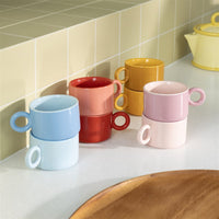 Colorful ceramic mugs stacked on a kitchen counter with a tiled wall background.