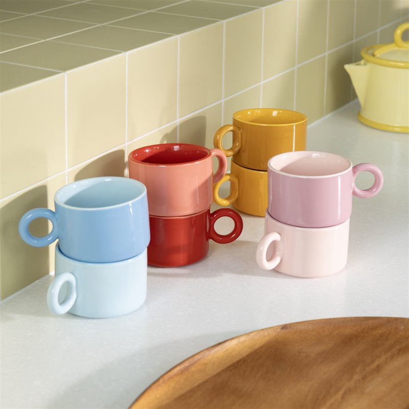 Colorful ceramic mugs stacked on a kitchen counter with a tiled wall background.