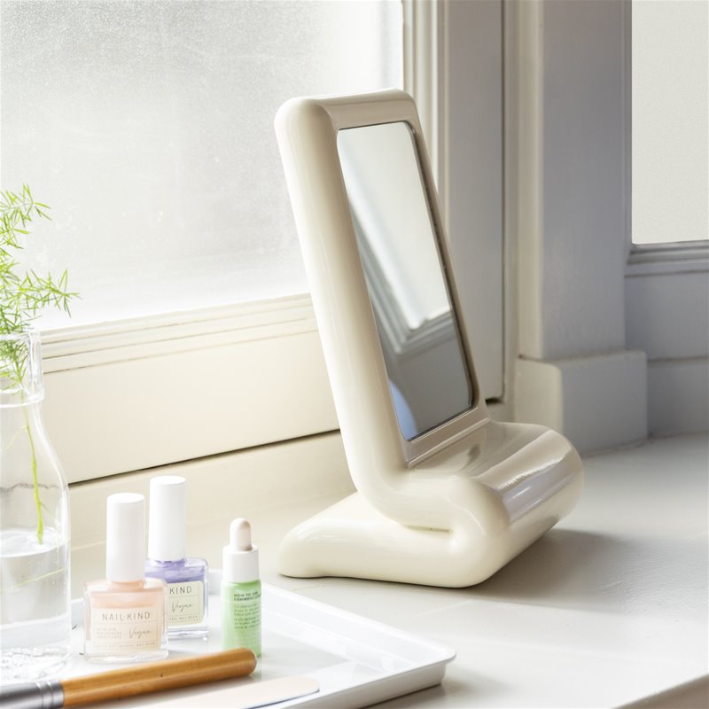 off-white sculptural vanity mirror on windowsill next to beauty essentials
