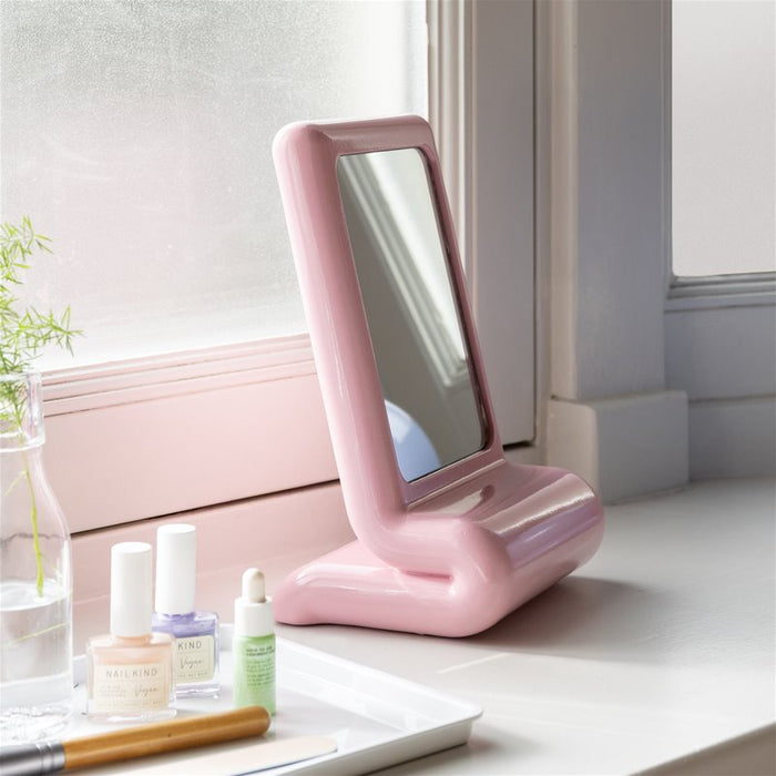 pink &k Amsterdam vanity mirror with chunky curved frame on a windowsill beside beauty items
