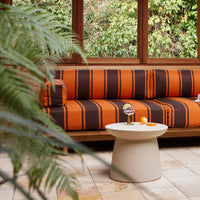 stoneware side table in cream white in front of an orange and brown striped sofa in a clean designed conservatory from hk living in scandinavian styling