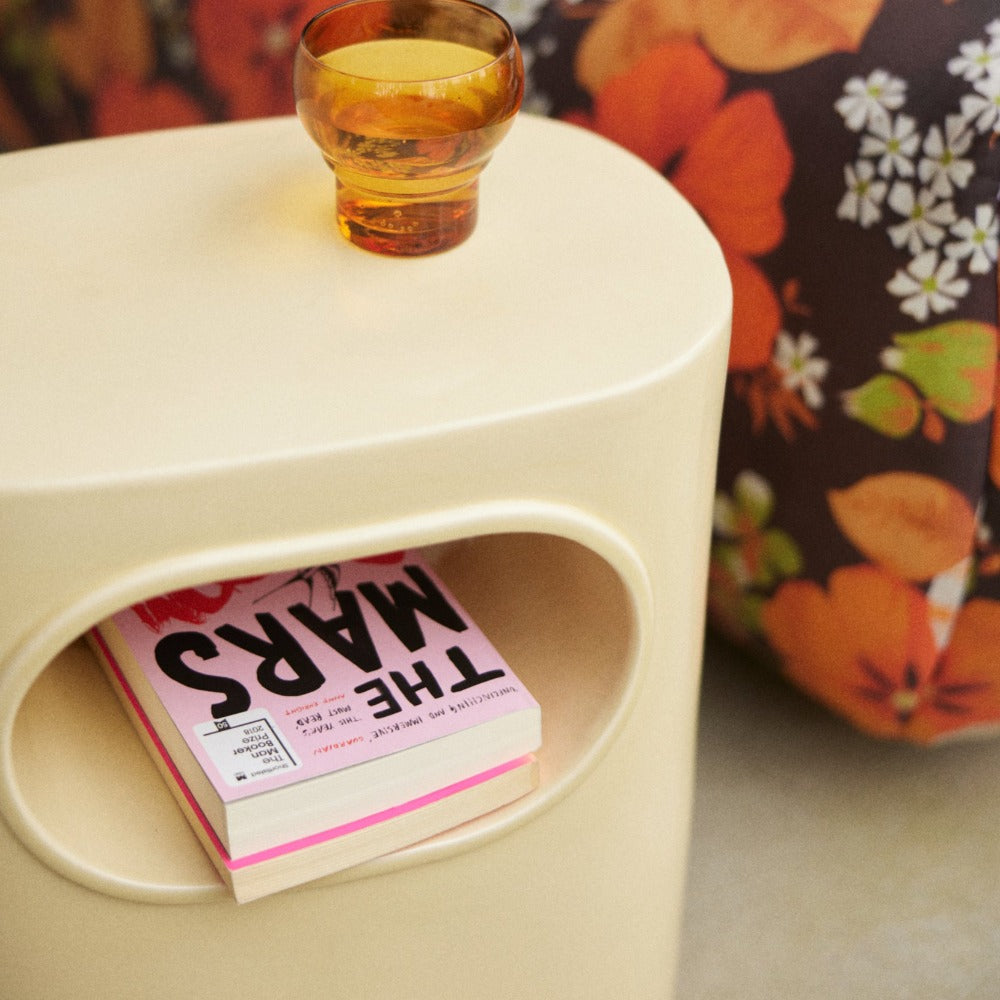 hkliving cream space side table with an amber coloured water glass and some pink covered books in its shelves