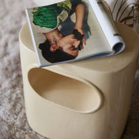 glossy cream side table with internal shelf which can be used of a stool tool from hkliving on a fluffy rug and with an open magazine on top revealing the image of a lady leaninig against a wall