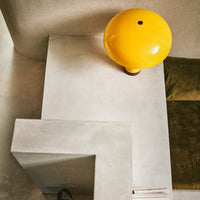 an egg yellow mushroom lamp sitting within a homescape of polished concrete giving it a flash of coour at the top of a step. with adark brown dot on the top and a dark caramel colar to the bottom of the lamp base