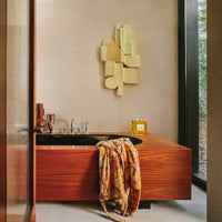 bathroomo scene with a geometric style nordic artwork on the wall behind the bath in a yellow beige cretaed in differing shapes and style with an almost boucle finish