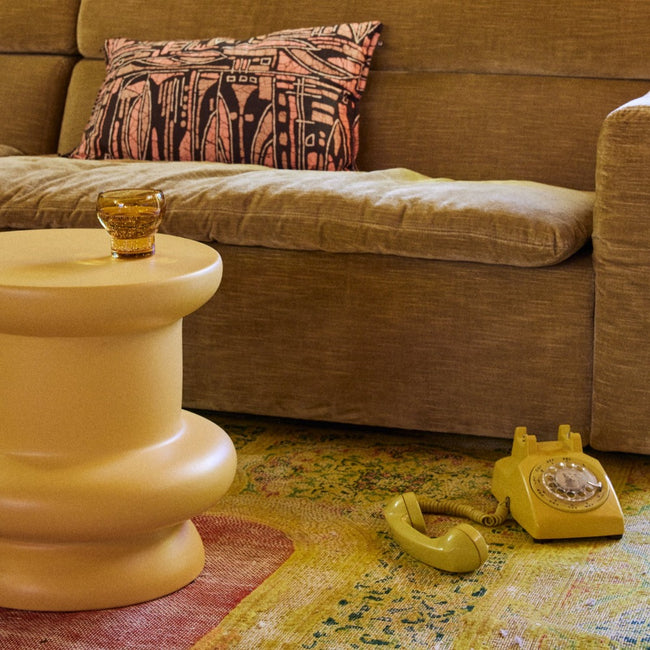 living room with brown sofa, yellow green rotary phone on a mottled rug, and an almost bobbin shapped yellow end table