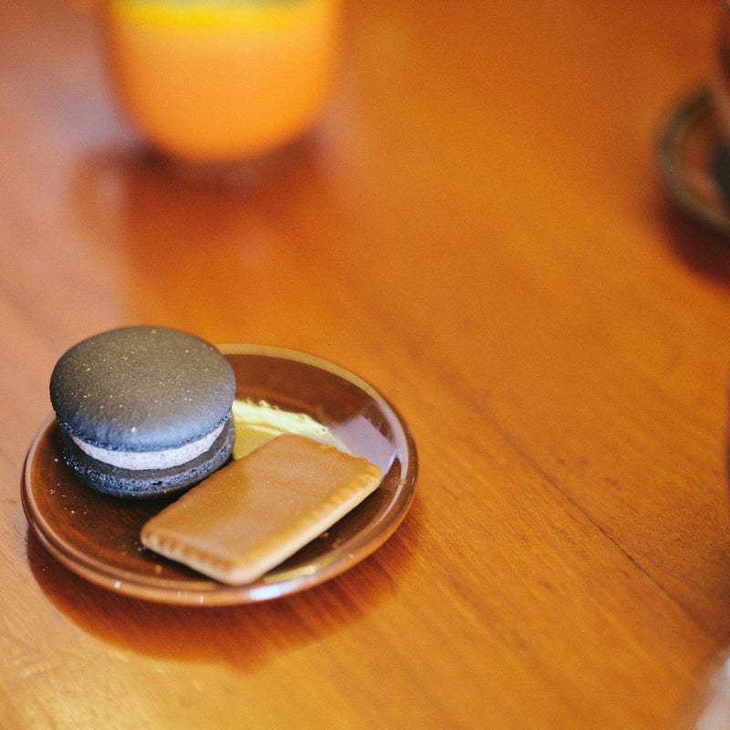 a single hkliving saucer with a macaron and biscuit sat apon it waiting on a wooden table top