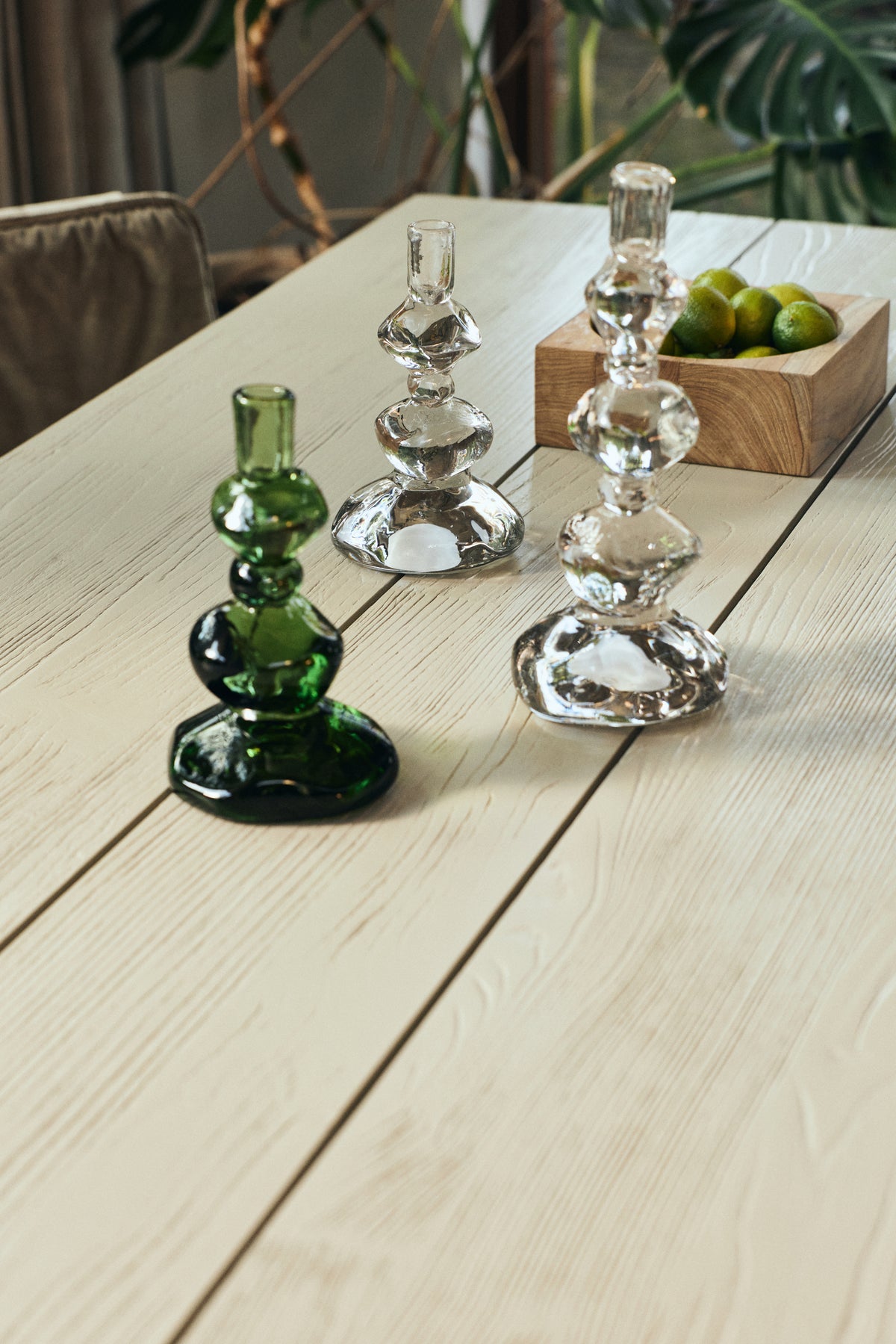 Clear and green Nienke Sikkema glass candle holders on a pale wooden dining table