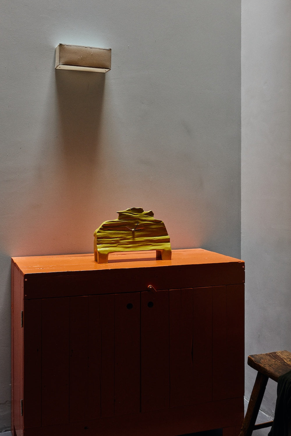 The HKLIVING chartreuse mantle clock on top of an orange sideboard beneath a wall-mounted reading light, with a wooden stool visible to the side