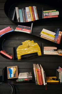 The HKLIVING chartreuse mantle clock displayed on a curved black wave-shaped bookshelf, surrounded by books and a small framed abstract painting