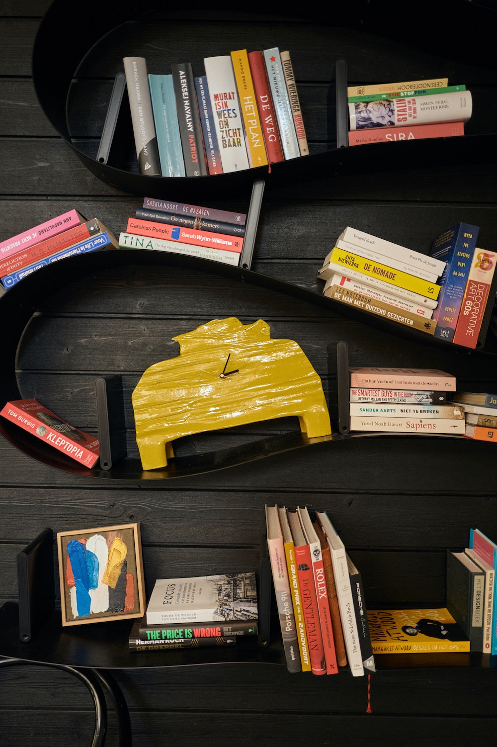 The HKLIVING chartreuse mantle clock displayed on a curved black wave-shaped bookshelf, surrounded by books and a small framed abstract painting