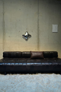 Chrome orb wall sculpture on a concrete wall above a black leather sofa, reflective statement wall decor